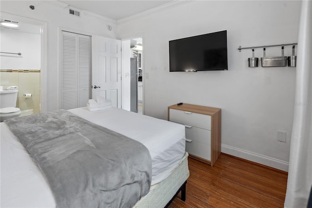 bedroom featuring visible vents, crown molding, wood finished floors, baseboards, and a closet