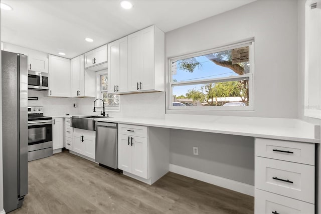 2014 10th St NW, Winter Haven, FL 33881 - kitchen featuring appliances with stainless steel finishes, a sink, built in desk, light wood-style flooring, and white cabinetry