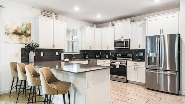 kitchen featuring white cabinets, dark countertops, stainless steel appliances, a peninsula, and backsplash