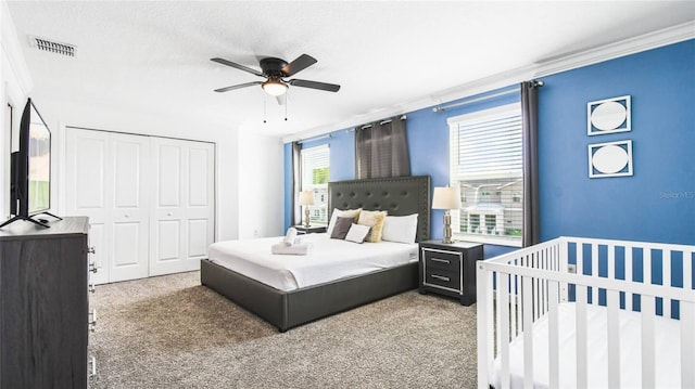 carpeted bedroom featuring visible vents, a ceiling fan, crown molding, and a closet