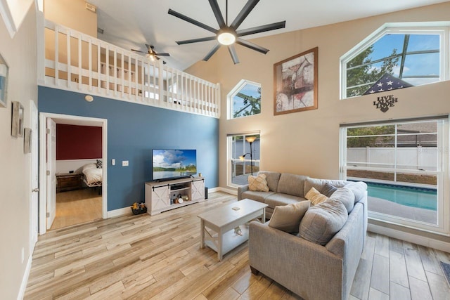 living area featuring baseboards, ceiling fan, a towering ceiling, and wood finished floors