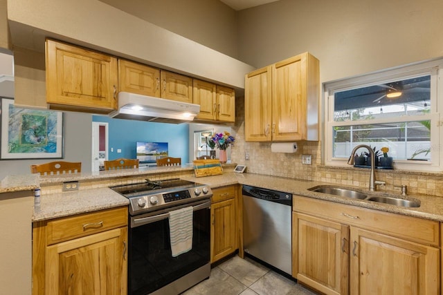 kitchen featuring a sink, stainless steel appliances, light stone countertops, backsplash, and under cabinet range hood