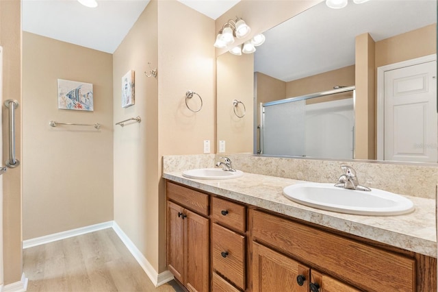 bathroom featuring double vanity, a shower stall, a sink, and wood finished floors