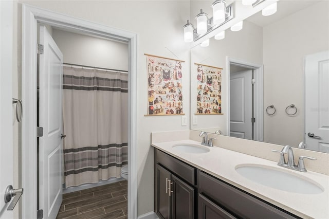 full bathroom featuring toilet, double vanity, wood finish floors, and a sink