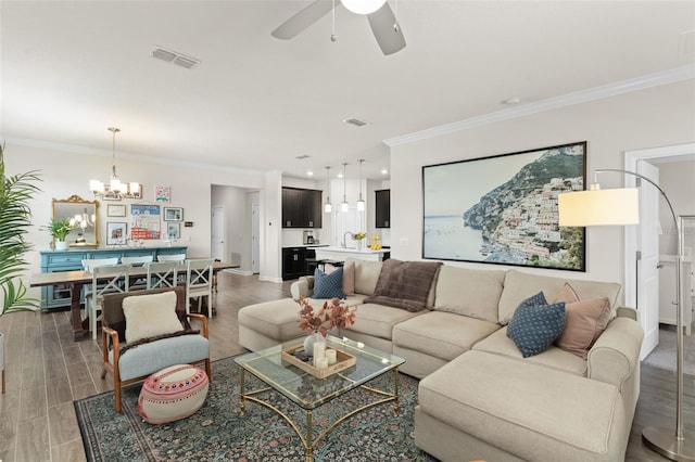 living area featuring visible vents, crown molding, wood finished floors, baseboards, and ceiling fan with notable chandelier