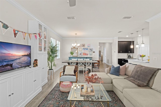 living area featuring visible vents, ornamental molding, light wood-style floors, and a chandelier