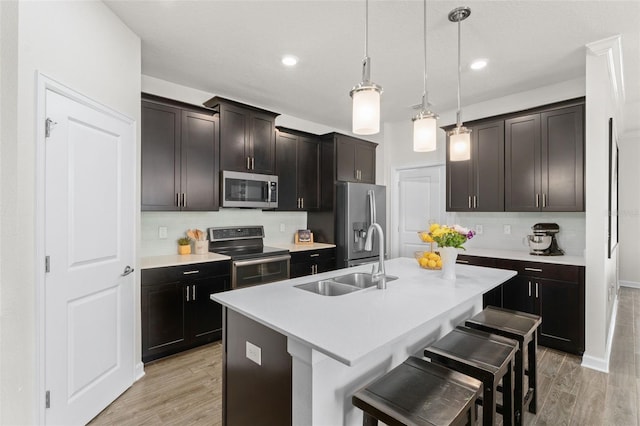 kitchen with a breakfast bar, a center island with sink, a sink, light wood finished floors, and stainless steel appliances