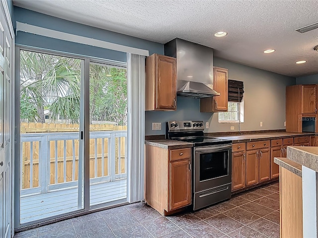 499 W Beresford Rd, Deland, FL 32720 - kitchen with stainless steel electric range, a textured ceiling, brown cabinetry, wall chimney exhaust hood, and dark tile patterned flooring