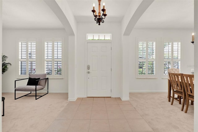 carpeted entryway featuring baseboards, arched walkways, tile patterned flooring, and an inviting chandelier