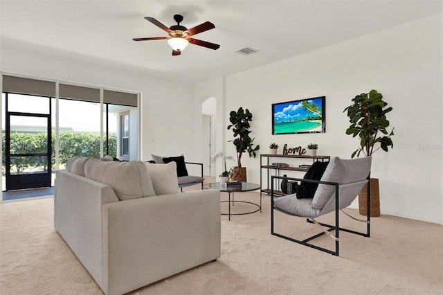 living area featuring arched walkways, visible vents, a ceiling fan, and light colored carpet