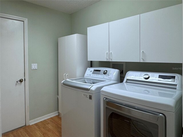 32900 Crooked Oaks Ln, Leesburg, FL 34748 - laundry room featuring light wood-style floors, cabinet space, washing machine and clothes dryer, baseboards, and a textured ceiling