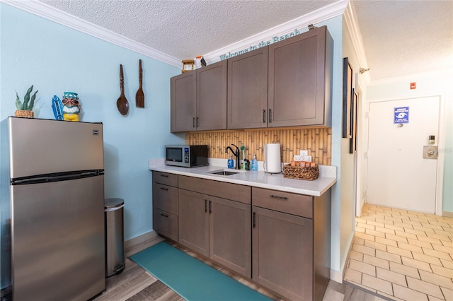 2043 S Atlantic Ave Unit 105, Daytona Beach Shores, FL 32118 - kitchen featuring a textured ceiling, crown molding, a sink, light countertops, and stainless steel appliances