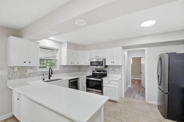 kitchen featuring appliances with stainless steel finishes, a sink, light countertops, a peninsula, and backsplash