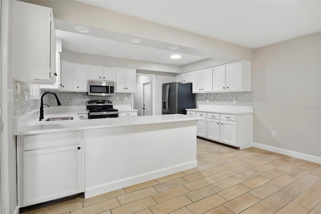 kitchen featuring backsplash, appliances with stainless steel finishes, a sink, a peninsula, and white cabinetry