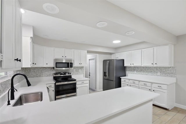 kitchen with a peninsula, light countertops, tasteful backsplash, a sink, and appliances with stainless steel finishes