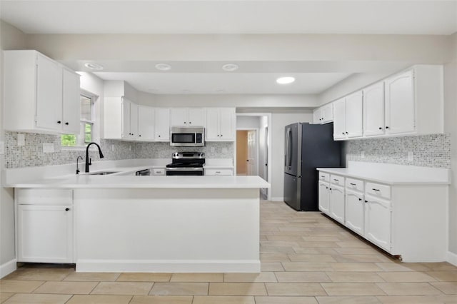 kitchen with appliances with stainless steel finishes, a sink, light countertops, a peninsula, and backsplash