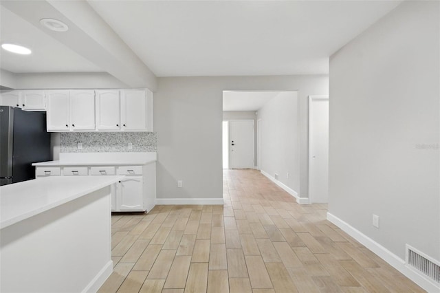 kitchen featuring visible vents, freestanding refrigerator, baseboards, light countertops, and white cabinets