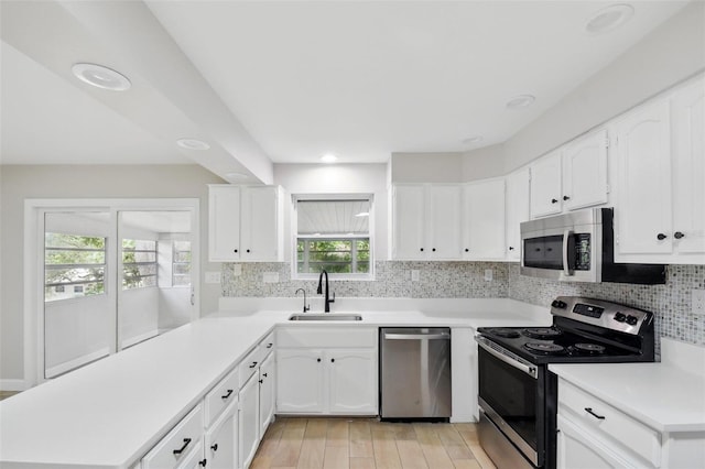 kitchen featuring a peninsula, light wood-type flooring, tasteful backsplash, a sink, and appliances with stainless steel finishes
