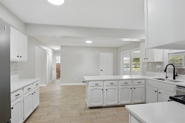 kitchen featuring a sink, tasteful backsplash, a peninsula, and white cabinetry