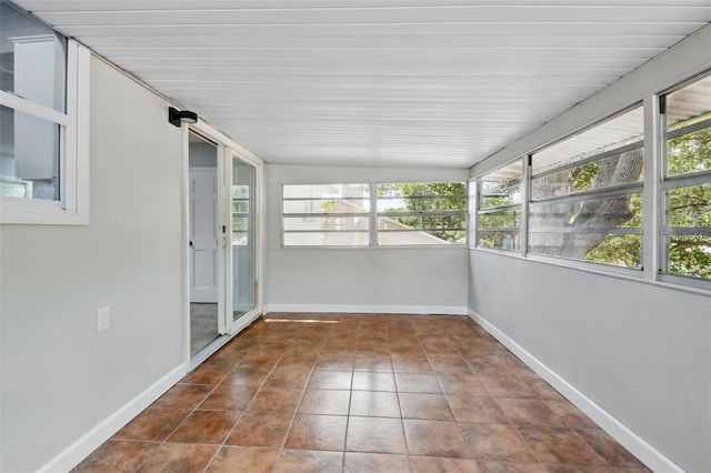 unfurnished sunroom featuring baseboards, tile patterned floors, and lofted ceiling