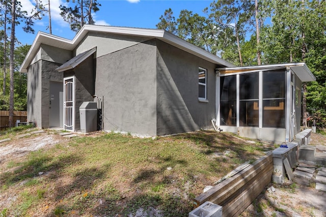 view of home's exterior featuring a sunroom, stucco siding, and fence