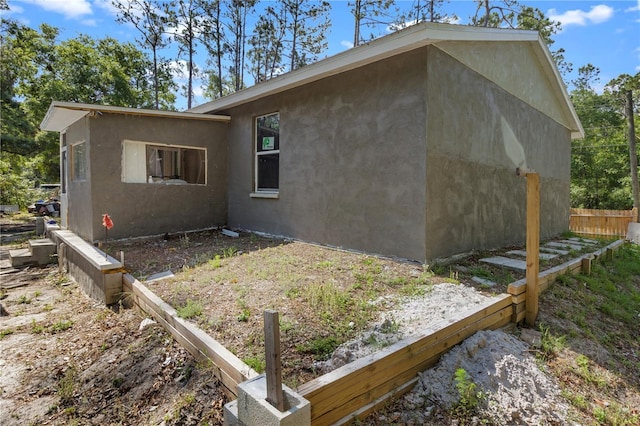 view of side of property with stucco siding and fence