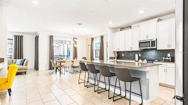 2936 Protagonist St, Kissimmee, FL 34746 - kitchen with a sink, a breakfast bar area, an island with sink, stainless steel microwave, and backsplash