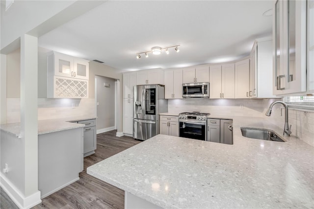 kitchen with light stone countertops, appliances with stainless steel finishes, a sink, wood finished floors, and backsplash