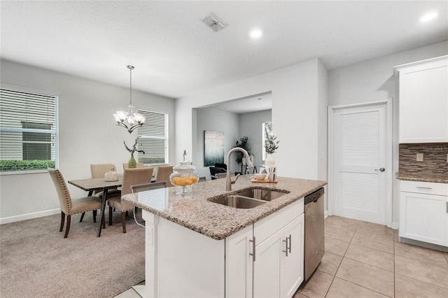 kitchen with light stone countertops, a sink, dishwasher, visible vents, and a center island with sink