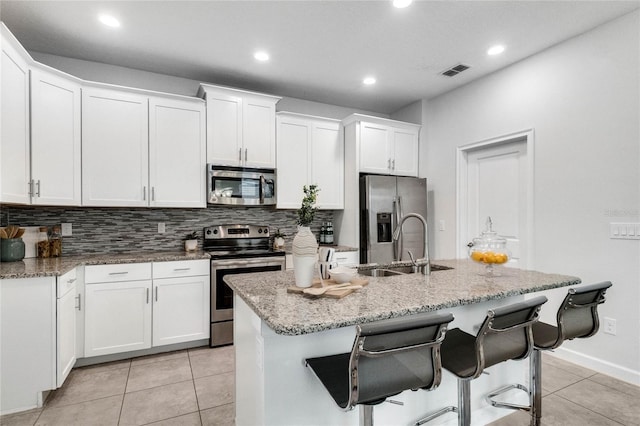 kitchen with decorative backsplash, an island with sink, white cabinets, light tile patterned floors, and stainless steel appliances