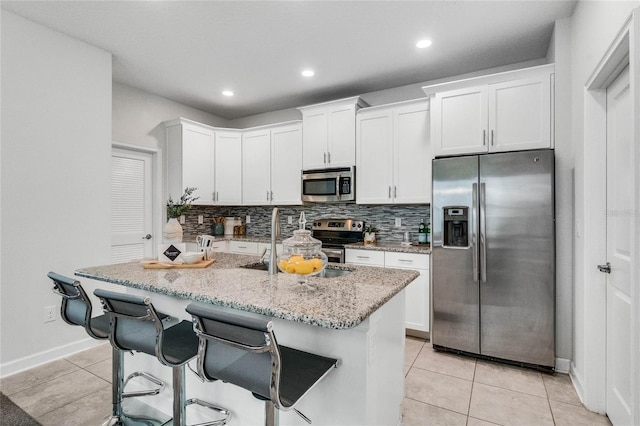 kitchen featuring light stone countertops, white cabinets, tasteful backsplash, appliances with stainless steel finishes, and light tile patterned floors