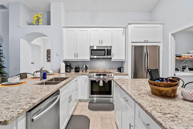 kitchen featuring independent washer and dryer, arched walkways, a sink, stainless steel appliances, and white cabinetry
