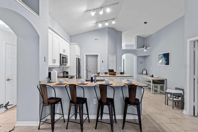 kitchen with appliances with stainless steel finishes, a breakfast bar, arched walkways, a peninsula, and white cabinetry