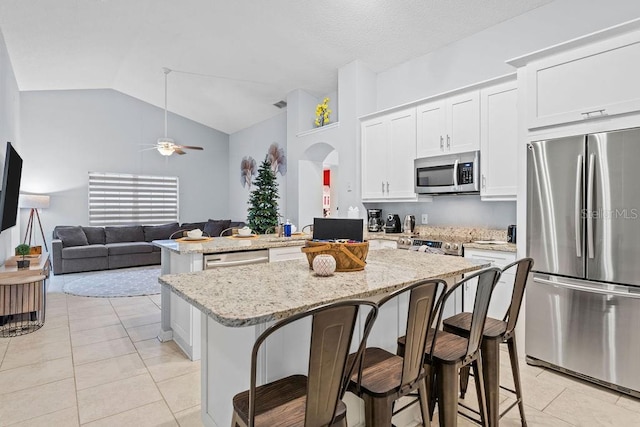 kitchen featuring a kitchen island, white cabinetry, arched walkways, light tile patterned floors, and stainless steel appliances