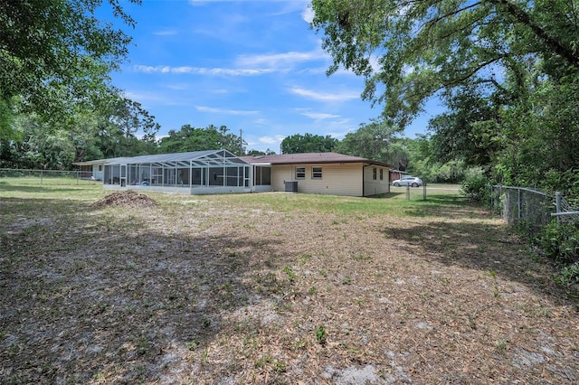 back of property with a sunroom, a fenced backyard, central AC, and a yard