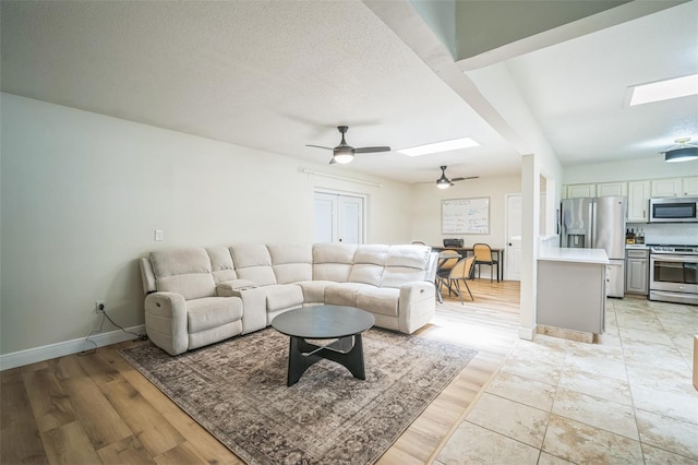 living area with ceiling fan, light wood-style floors, a textured ceiling, baseboards, and a skylight