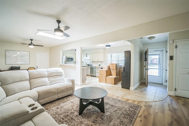 living area with baseboards, a ceiling fan, a textured ceiling, and light wood-style flooring