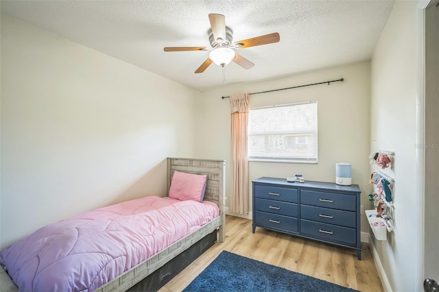 bedroom featuring baseboards, a ceiling fan, light wood finished floors, and a textured ceiling