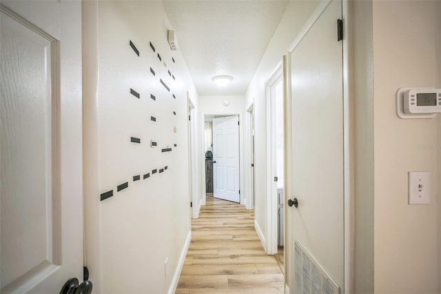 hall with baseboards, light wood-type flooring, a textured ceiling, and visible vents