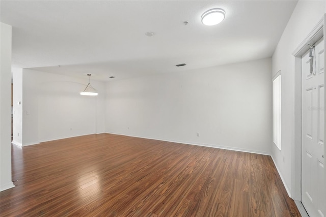 empty room featuring baseboards, dark wood-style floors, and visible vents