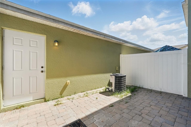 view of exterior entry with a patio area, stucco siding, fence, and cooling unit