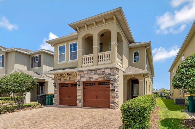view of front of house with stone siding, cooling unit, decorative driveway, stucco siding, and an attached garage