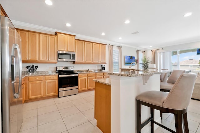kitchen with a kitchen bar, appliances with stainless steel finishes, light stone counters, ornamental molding, and light tile patterned flooring
