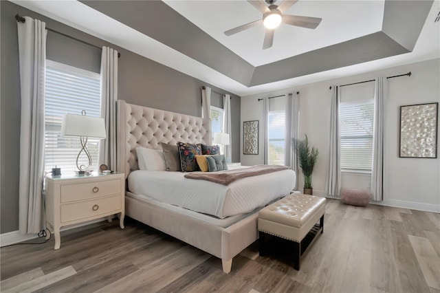 bedroom featuring light wood-type flooring, baseboards, ceiling fan, and a tray ceiling