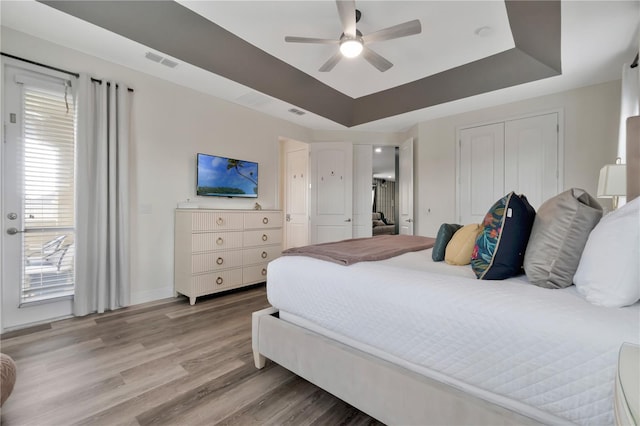 bedroom with a raised ceiling, baseboards, light wood-type flooring, visible vents, and a closet