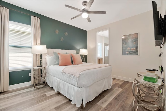 bedroom featuring ceiling fan, baseboards, an accent wall, and light wood-style flooring