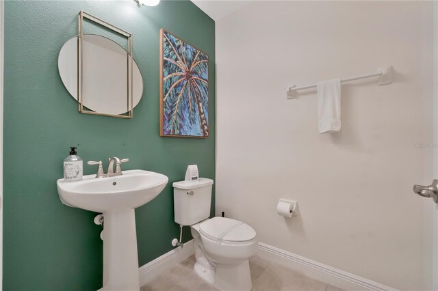half bath with baseboards, tile patterned floors, and toilet