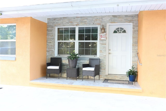 entrance to property featuring covered porch, stucco siding, and stone siding