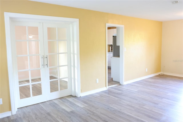 empty room with baseboards, french doors, and light wood-style flooring