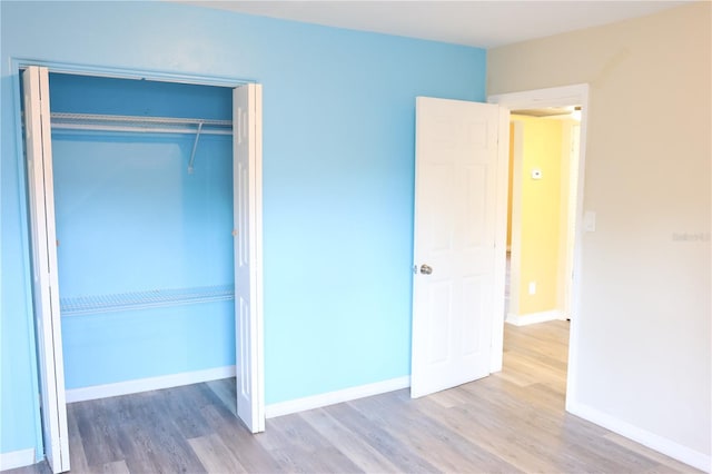 unfurnished bedroom featuring baseboards, wood finished floors, and a closet